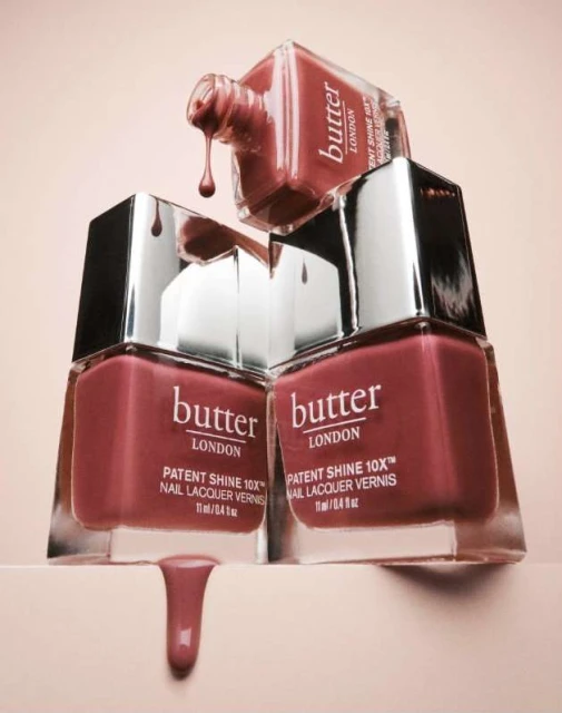 Close-up studio shot of Butter London nail polish bottles stacked with drips of nail lacquer, emphasizing color and shine for beauty advertising.