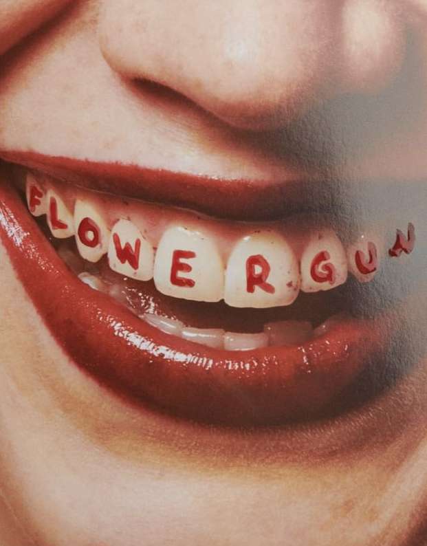 Close-up of a woman's smile with red lipstick and the words 'Flower Guy' written in red on her teeth for a unique effect.