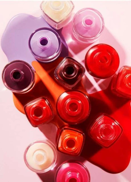 Overhead shot of a variety of open nail polish bottles in red, pink, orange, yellow, and purple, with spilled polish on a pink surface.