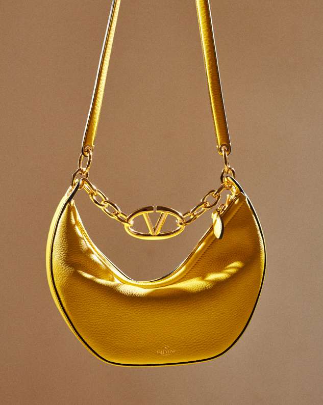 Elegant Valentino Garavani handbag in yellow leather with gold chain and logo detail, presented against a soft tan background.
