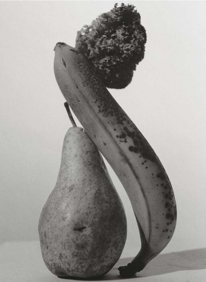 Monochrome still life photo of a banana, pear, and leafy vegetable against a plain backdrop, highlighting textures and contrasts.