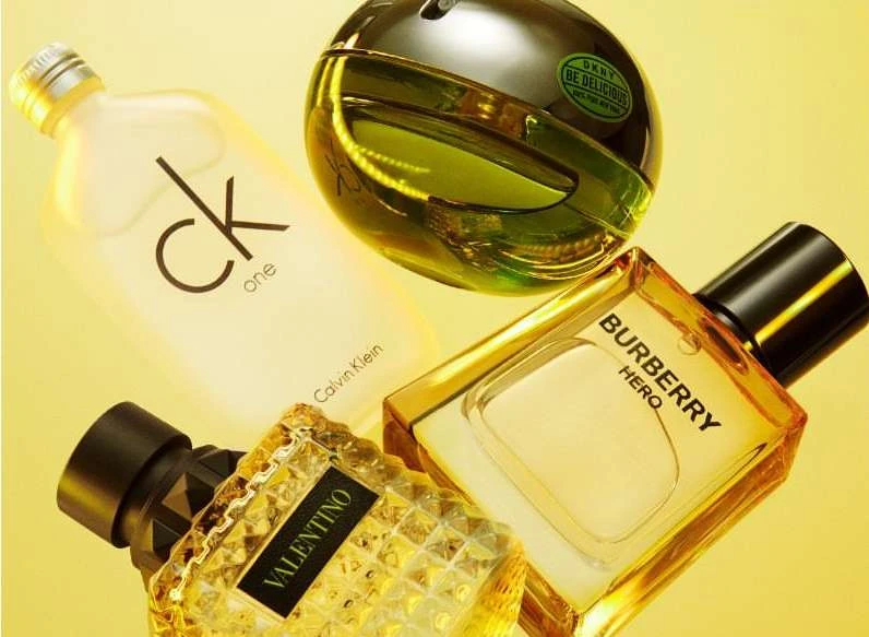 Close-up studio shot showcases Calvin Klein, Burberry, Valentino, DKNY perfume bottles in a visually appealing layout against yellow backdrop.