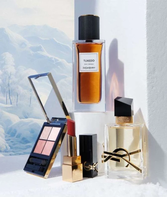 Still life shot of YSL beauty products: perfume bottles, lipstick, and eyeshadow palette against a snowy mountain backdrop.