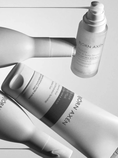 Björn Axén hair care products in white bottles, including moisture hair and scalp serum and mask, arranged in a minimalist still life.