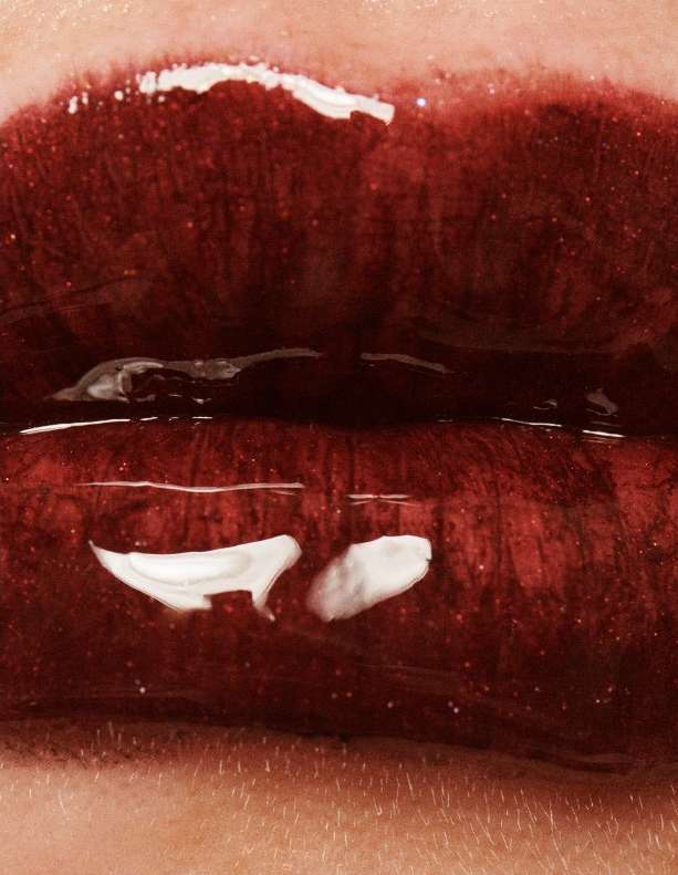 Close-up shot of open red lips with glossy lipstick and visible skin texture around the mouth in a vertical, macro studio shot.
