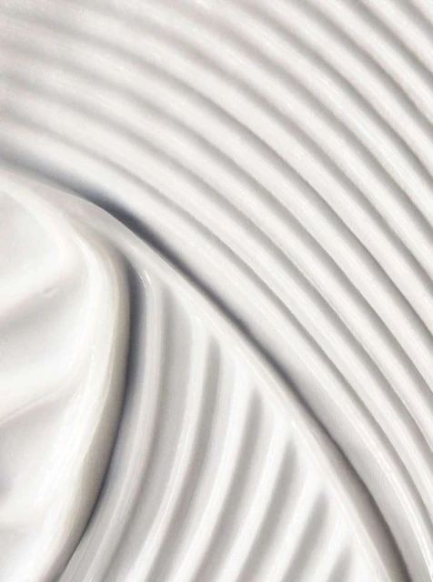 Close-up of white cream with a textured surface featuring a pattern of parallel lines and smooth, glossy waves.