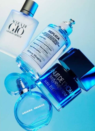 Four perfume bottles from different brands sit on a light blue background, including Ariana Grande, Giorgio Armani, and Yves Saint Laurent.