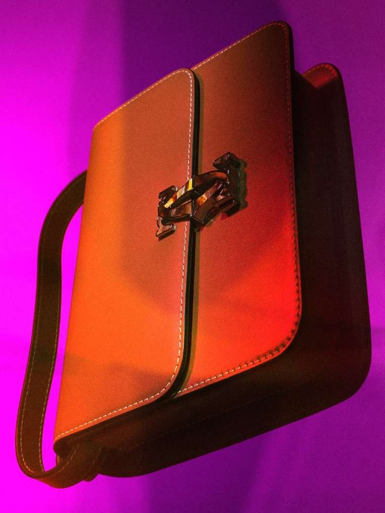 Studio shot of a brown leather satchel handbag with metal hardware against a vibrant purple backdrop, product photography, fashion accessory.