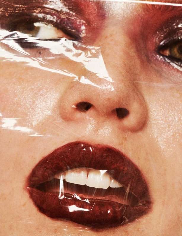 Close-up portrait of a female face covered in plastic wrap, featuring red lipstick and detailed eye makeup. Beauty and fashion aesthetic.
