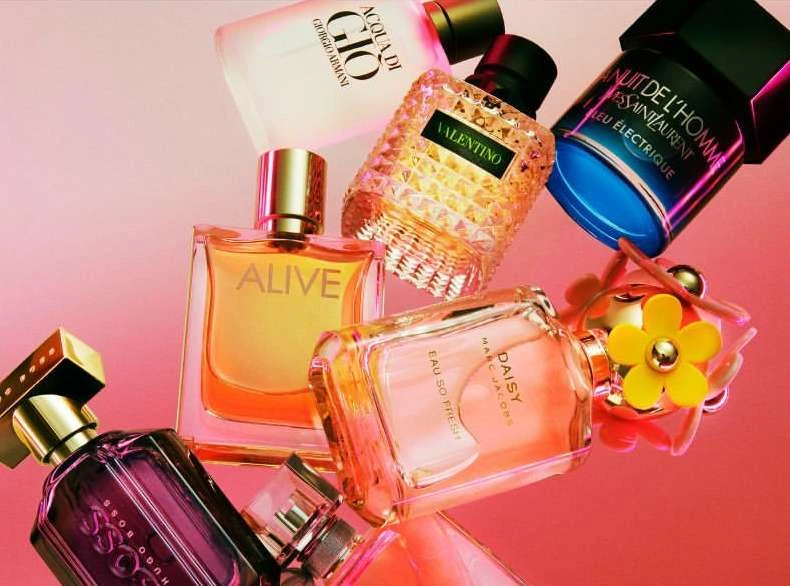 Assorted perfume bottles including Giorgio Armani Acqua di Gio, Valentino, and Hugo Boss, arranged on a reflective pink surface.