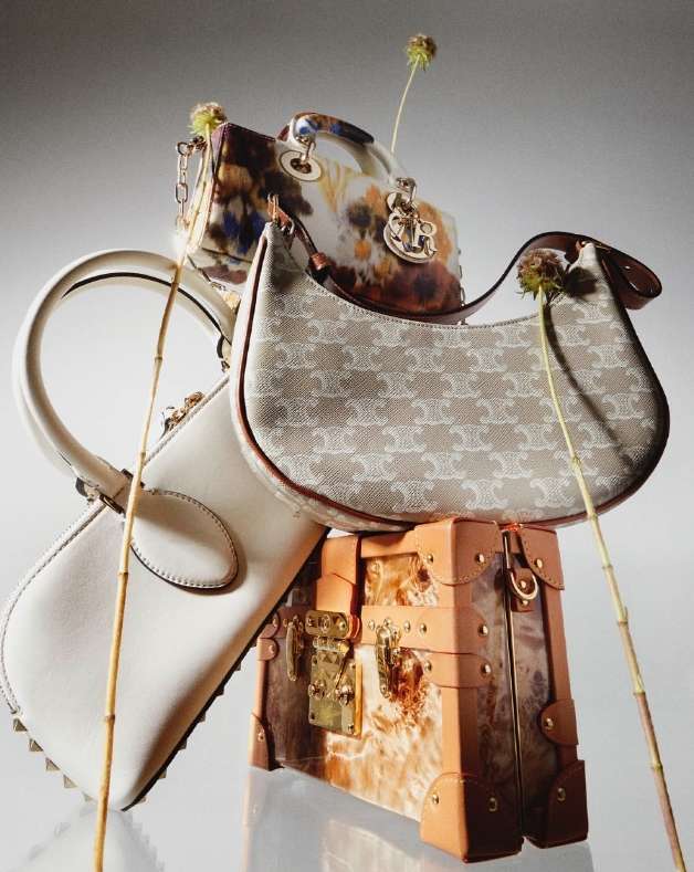 Still life studio shot featuring a stack of luxury handbags and a small trunk, each exhibiting unique textures, patterns, and colors.