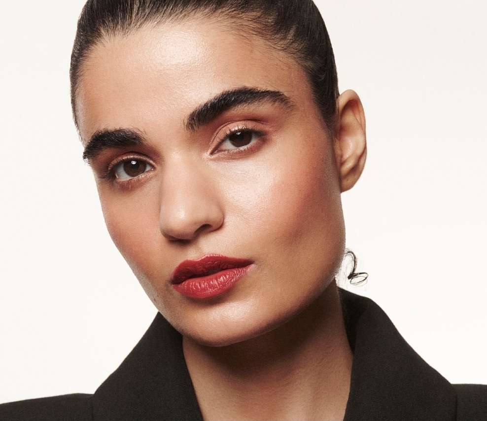 Close-up portrait of a woman with red lipstick and dark hair wearing a black blazer against a white background in a studio setting.