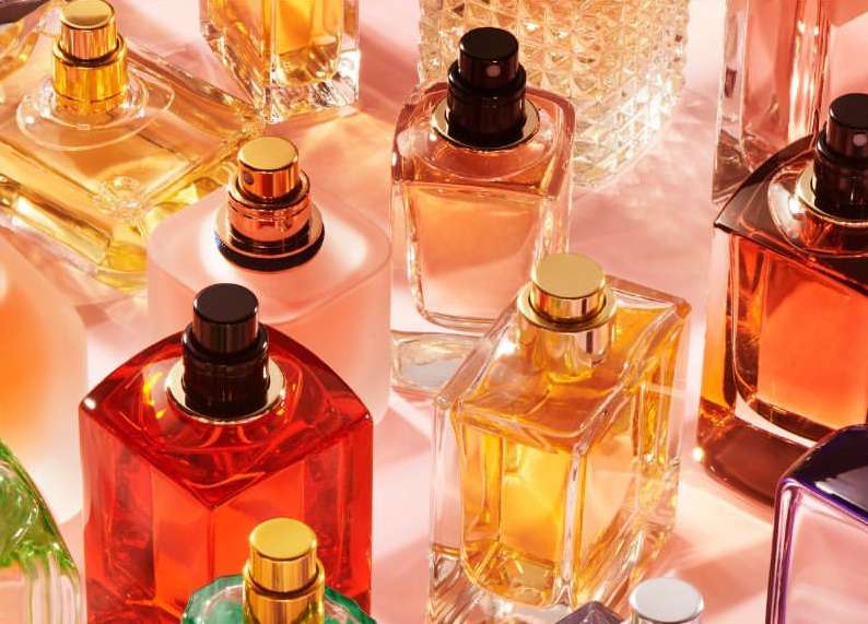 Still life close-up of several glass perfume bottles with various shapes, sizes, and colors on a light pink background, product shot.