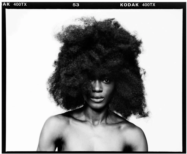 Striking monochrome portrait of a Black woman with an afro, showcasing her face and upper torso against a stark white background with film border.