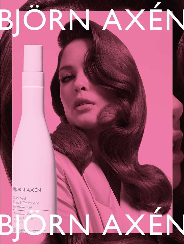 Beauty shot of a woman with wavy brown hair and a hair product bottle, pink background with Bjorn Axen text.