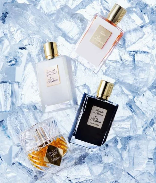 Four Kilian perfume bottles: amber, white, black, and clear, displayed on a bed of crushed ice, reflecting luxury and coolness.