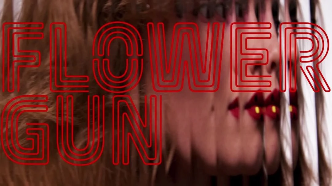 Portrait of a woman with red lipstick and blond wavy hair, partially obscured by red text that reads, 'FLOWER GUN'.