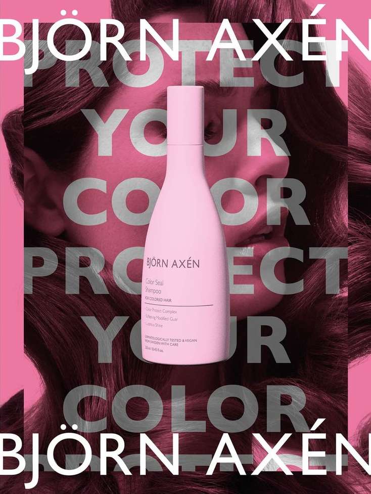 Bjorn Axen haircare product bottle, pale pink color, shown against a background of a woman with long wavy brown hair.