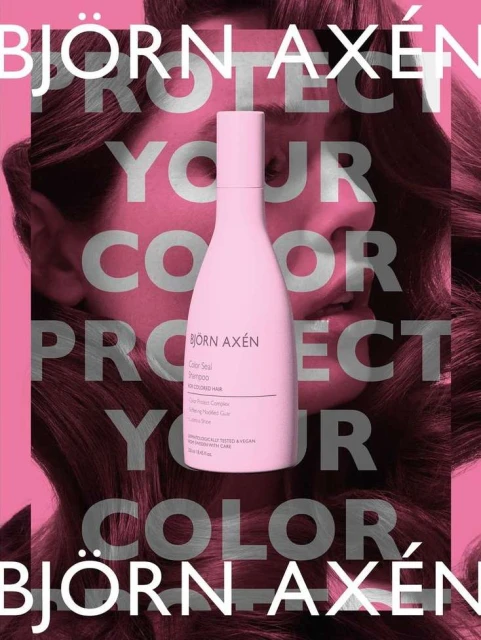 Bjorn Axen haircare product bottle, pale pink color, shown against a background of a woman with long wavy brown hair.