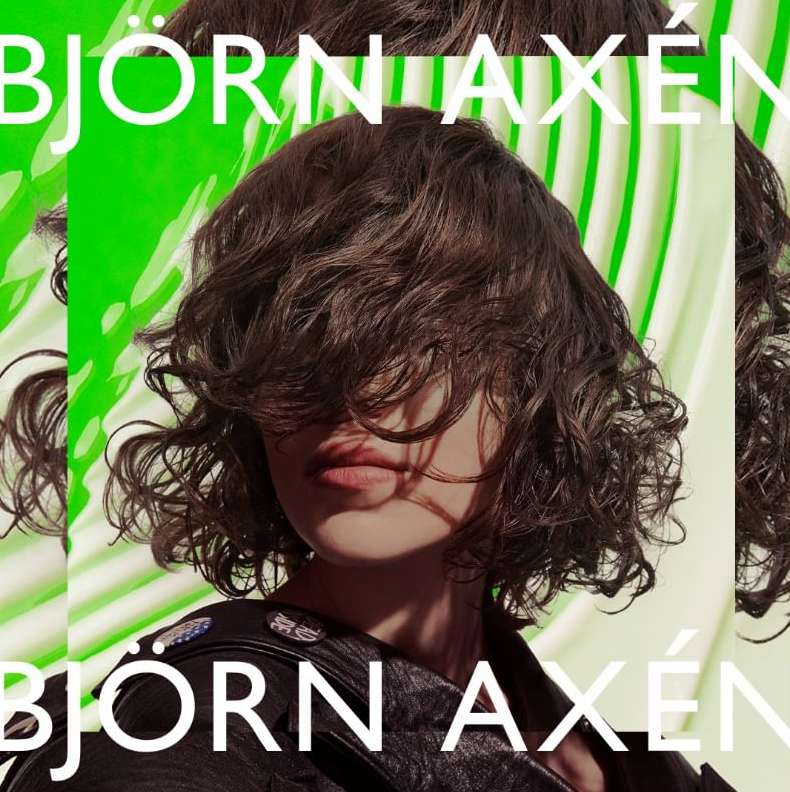 Portrait of a woman with wavy hair partially obscuring her face, wearing a black jacket, against a green and white background.