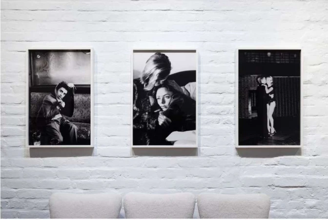 Three framed black and white portrait photographs hung on a painted white brick wall above three modern chairs