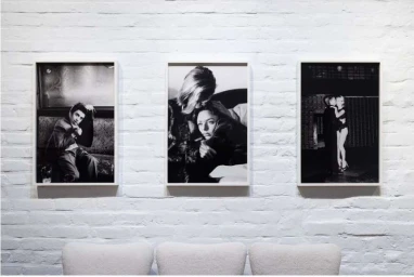 Three framed black and white portrait photographs hung on a painted white brick wall above three modern chairs