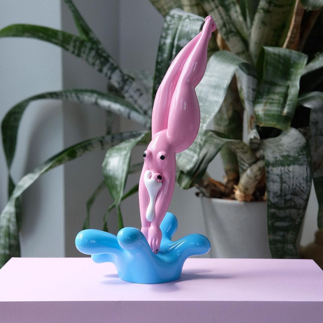 Pink human-like figure with blue splash on a pink table in front of a snake plant creates a playful, modern, and surreal art scene.