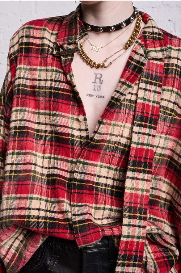 Close-up of person wearing a red and beige plaid shirt, accessorized with layered gold necklaces and a studded black choker.