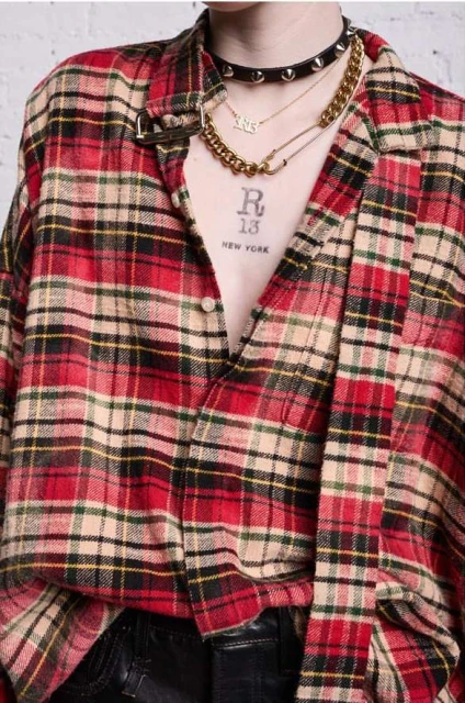 Close-up of person wearing a red and beige plaid shirt, accessorized with layered gold necklaces and a studded black choker.