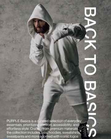 Man in white hoodie and sweatpants with hand wraps striking a boxer pose against a mottled grey background, looking at the camera.