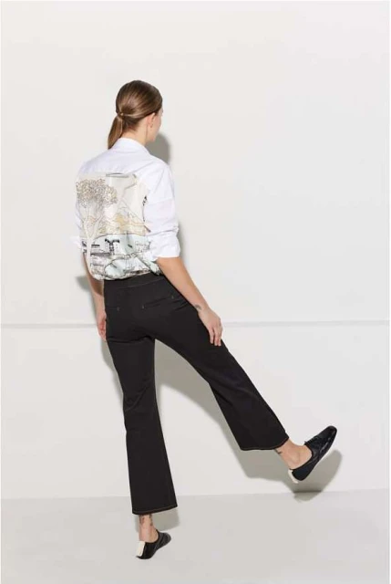 Back view of a stylish adult woman in black pants and a white shirt with a graphic design, striking a dynamic pose against a white backdrop.