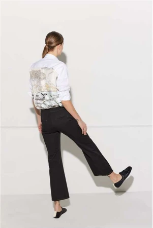 Back view of a stylish adult woman in black pants and a white shirt with a graphic design, striking a dynamic pose against a white backdrop.