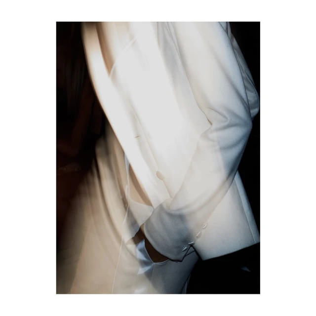 Fashion shot featuring the clean lines of a white blazer against a dark backdrop, highlighting texture and modern style.