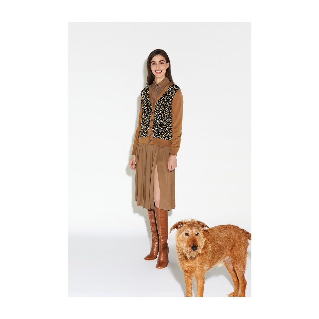 Full-length shot of a smiling woman in a cardigan and skirt standing with a dog against a white background in a studio.