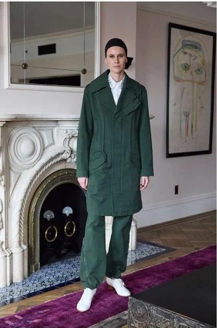Full-length shot of a slender young adult female standing in a modern room wearing an green coat with matching pants and white boots.