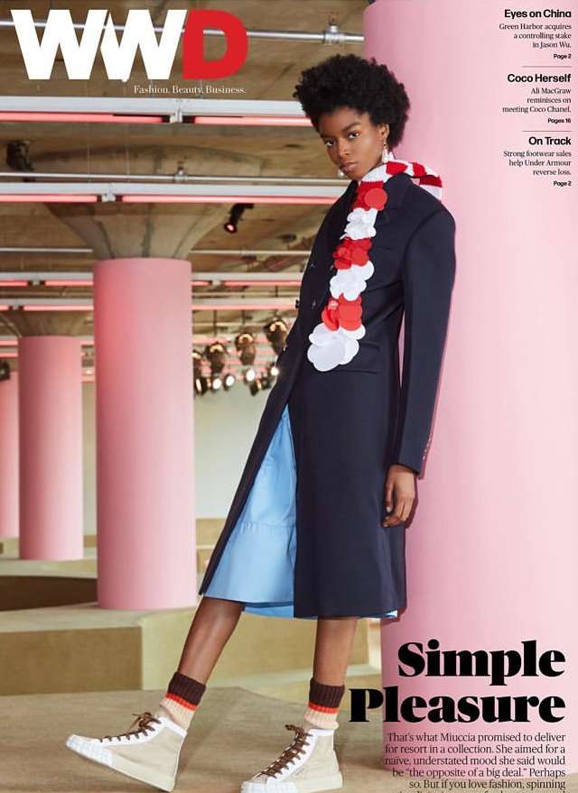WWD fashion magazine cover featuring a Black woman model wearing a long blue coat, a ruffled neckpiece, and sneakers on a pink catwalk.