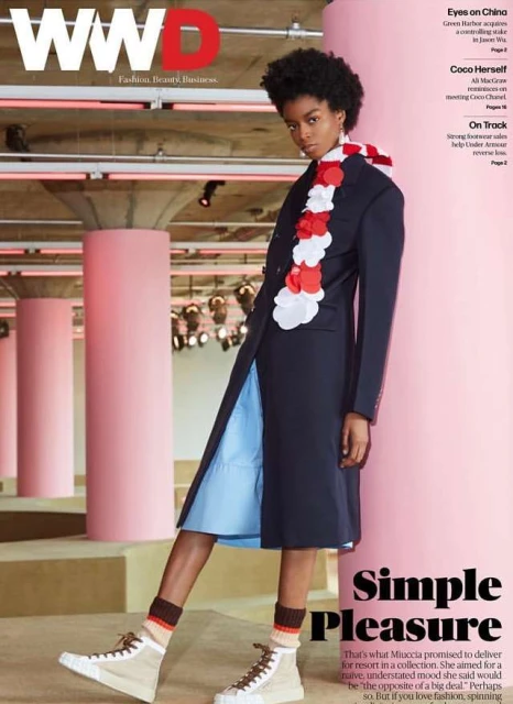 WWD fashion magazine cover featuring a Black woman model wearing a long blue coat, a ruffled neckpiece, and sneakers on a pink catwalk.