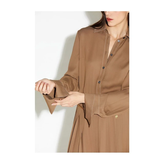 Woman in a light brown shirt dress and gold chain belt poses in a studio with a white backdrop. Fashion shoot.