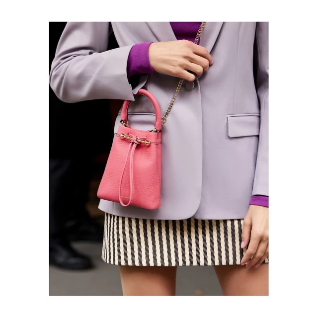 Woman in blazer carries a pink leather bucket bag with a chain strap and striped skirt, showcasing fashion and style.