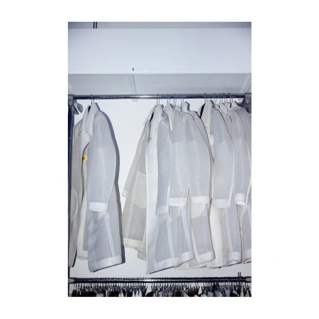 Rack of white lab coats or dust coats on hangers under fluorescent lighting, ready for use in a medical or cleanroom setting.