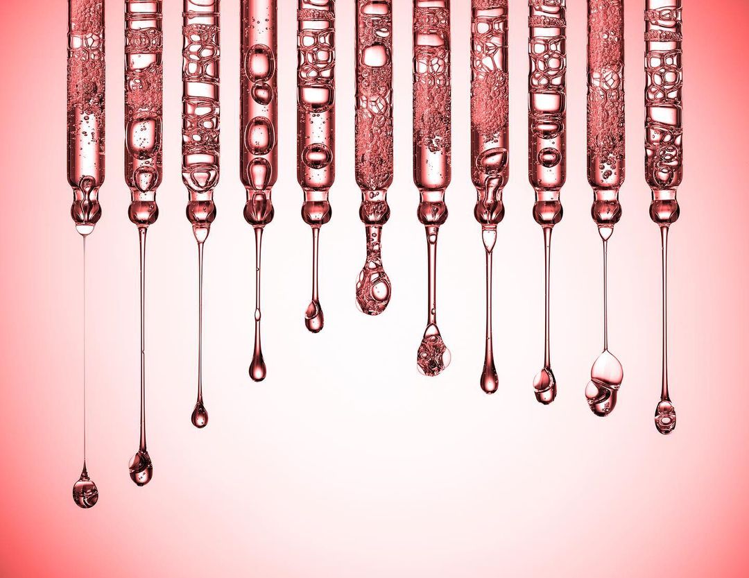 Close-up of water drops in glass tubes creating a visually appealing abstract arrangement against a gradient pink background.