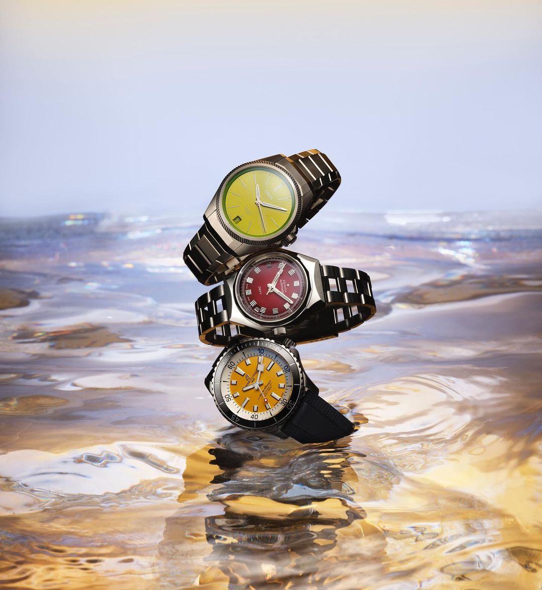 Three wristwatches stacked on top of each other, balanced in a vertical display against a blurred, colorful background.