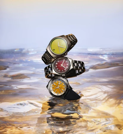 Three wristwatches stacked on top of each other, balanced in a vertical display against a blurred, colorful background.