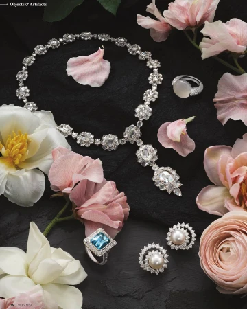 Elegant jewellery set including necklace, earrings, and rings arranged with light pink and white flowers against a dark background.