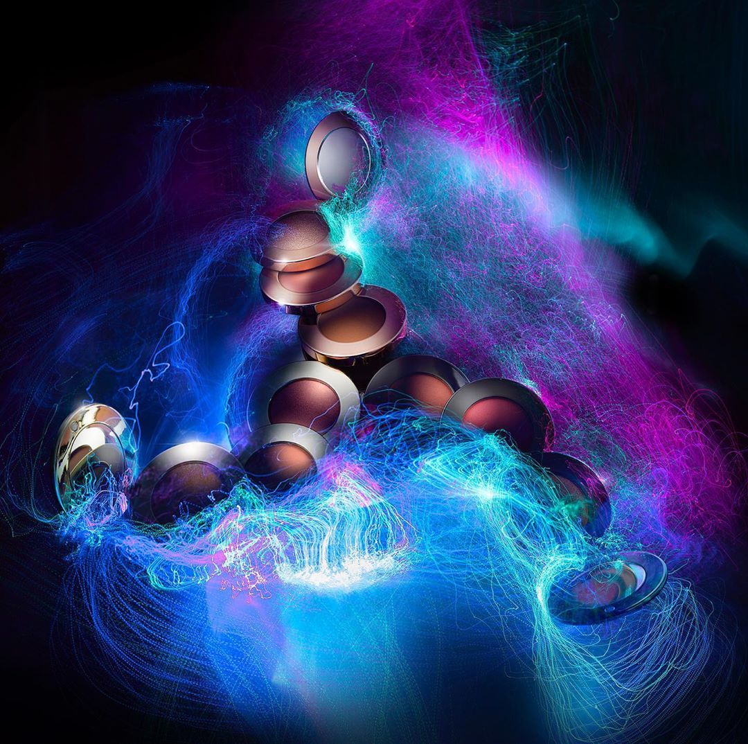 Dramatic still life of makeup compacts with glowing light trails of blue and purple on a dark background, beauty and cosmetics.