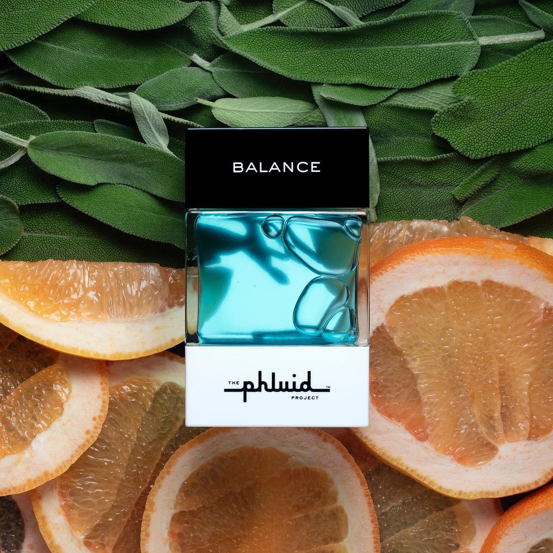 Product shot of Balance by The Phluid Project, a turquoise fragrance bottle set among leaves and citrus slices, creating a refreshing vibe.