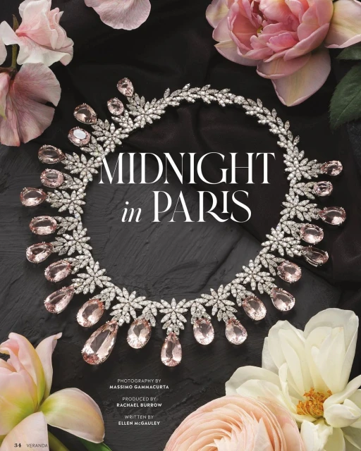 Close-up of a diamond and light pink gemstone necklace surrounded by pink and white flowers on a dark grey stone surface.