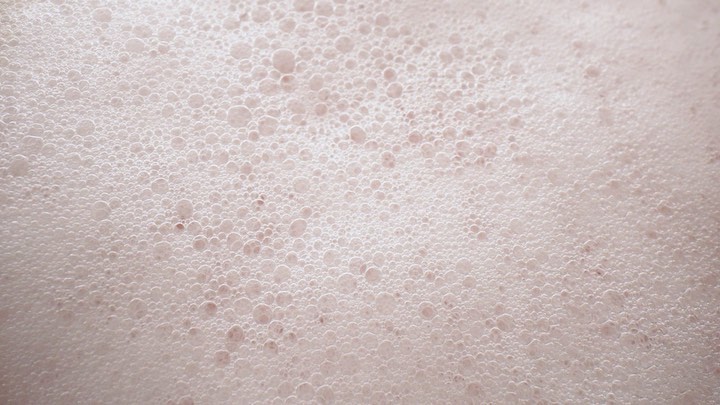 Close-up of pale pink foam with tiny bubbles creates a soft, textured surface, perfect for backgrounds or abstract visuals.