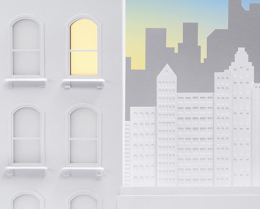 Minimalist paper art featuring an urban cityscape, showcasing white buildings with arched windows and a distant grey skyline under a gradient sky.