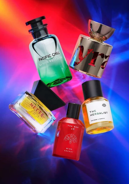 Still life shot of assorted perfume bottles, including brands like Louis Vuitton and The Herbalist, set against a vibrant, dynamic backdrop.